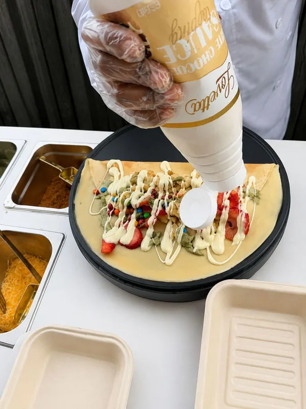 Fresh crepe being topped with chocolate and whipped cream